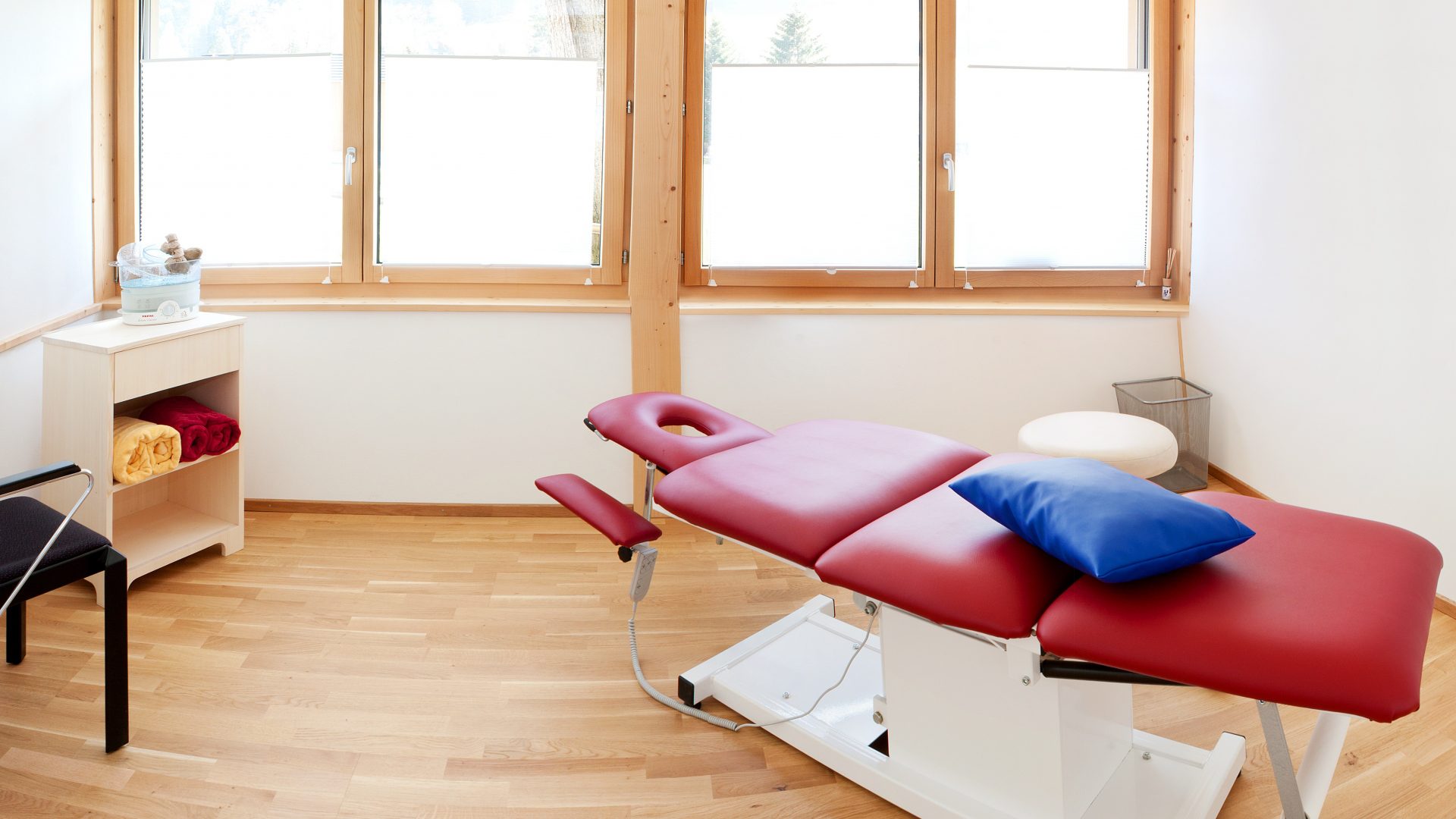 Heller Behandlungsraum mit roter Therapieliege in der Naturheilpraxis